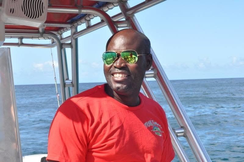 Captain Brandon Bruce smiling at the helm of the boat in his red Fish Tobago shirt