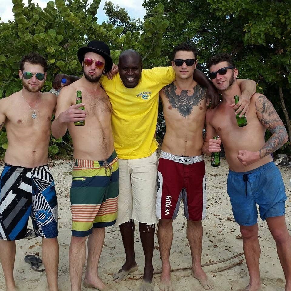 The Fish Tobago guide in his yellow crew shirt, arms around four smiling guests on the beach