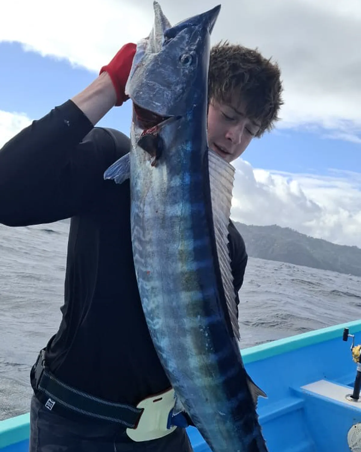 A young angler holding up a wahoo, Tobago's hills on the horizon